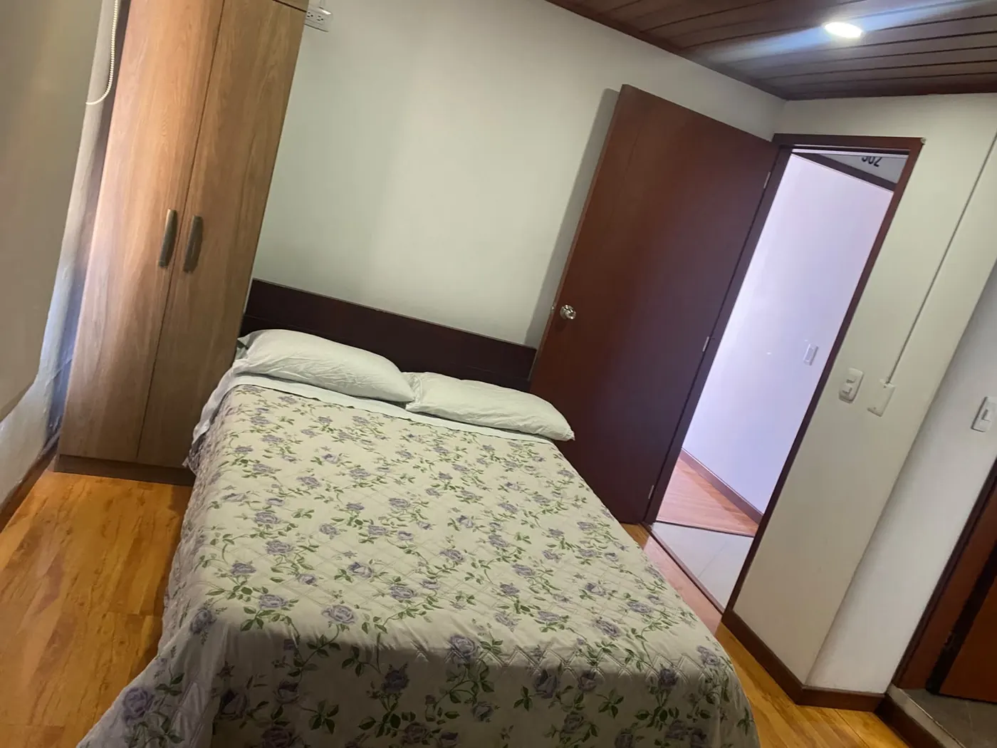 Cama doble con cubrecama floral y closet de madera